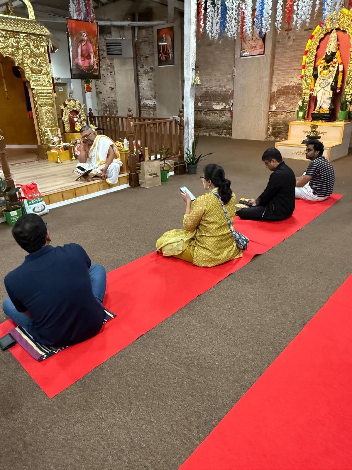 Devotees seated on red carpets facing the shrine