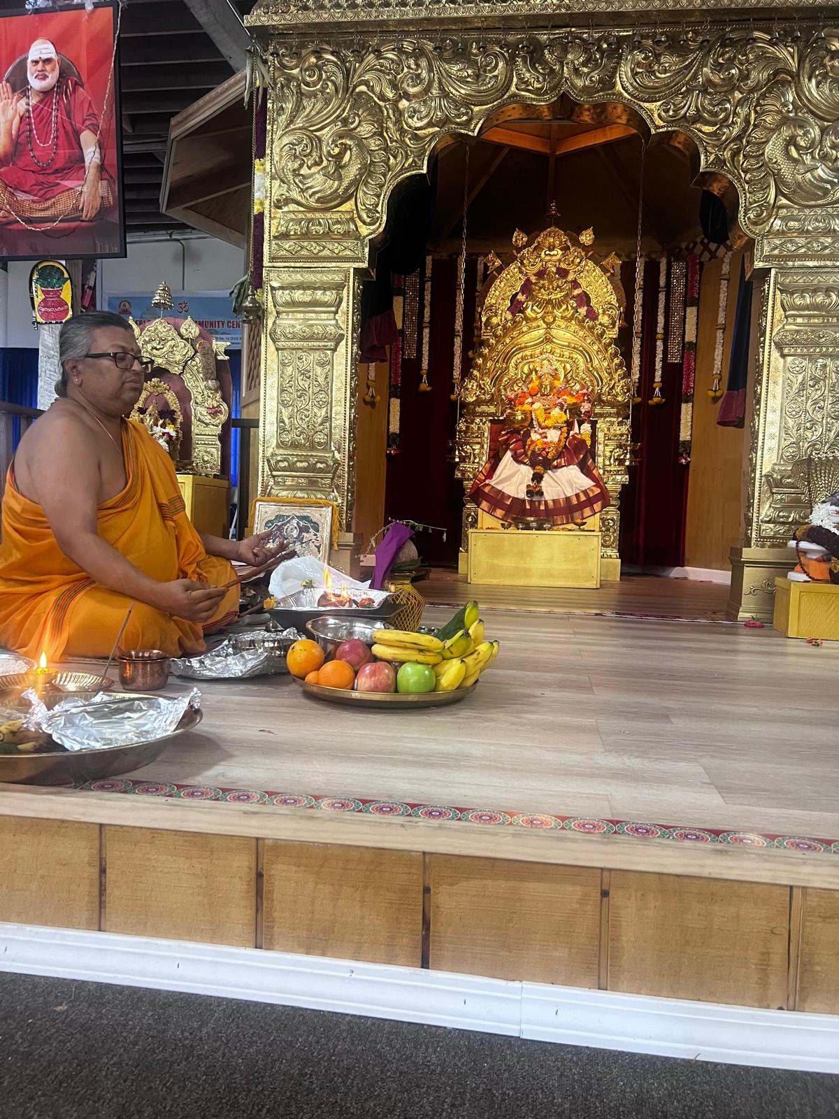 Priest seated in front of the shrine with fruit offerings